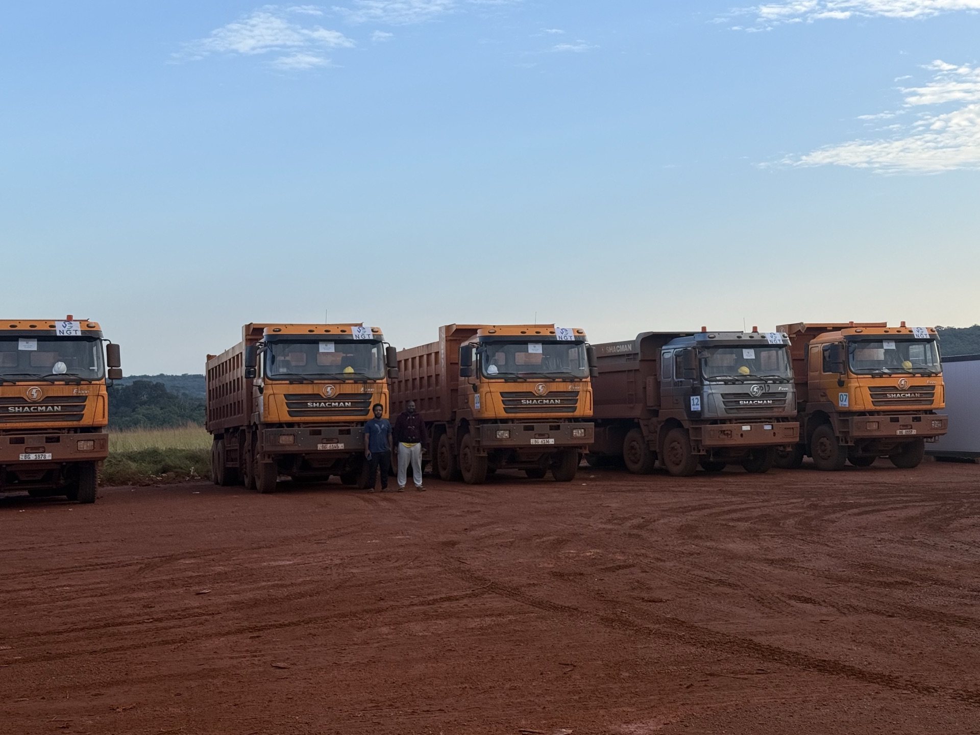Trucks lined up against a backdrop of green Guinean hills